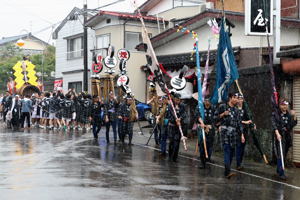 雨の中、筒引きを行う若者の画像