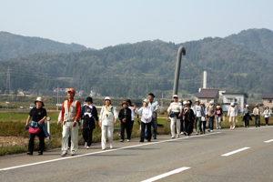 田んぼの脇の道路を歩く参加者の画像