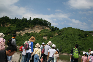 河原の対岸にできた地層を皆で見ている画像