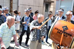 太鼓を叩く96歳の男性とそれを見守る100歳の男性の画像