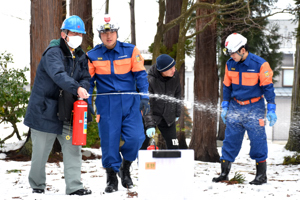 消防団員の補助を受けながら消火器操作訓練を行う男性の画像