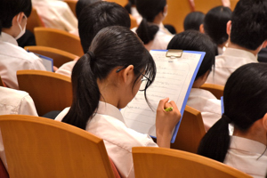 講話の内容をメモする中学生の画像