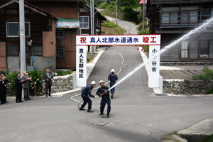 真人北部水道通水式で放水をする消防団の画像