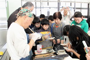 素焼きされた器に筆で模様を描く小学生の画像